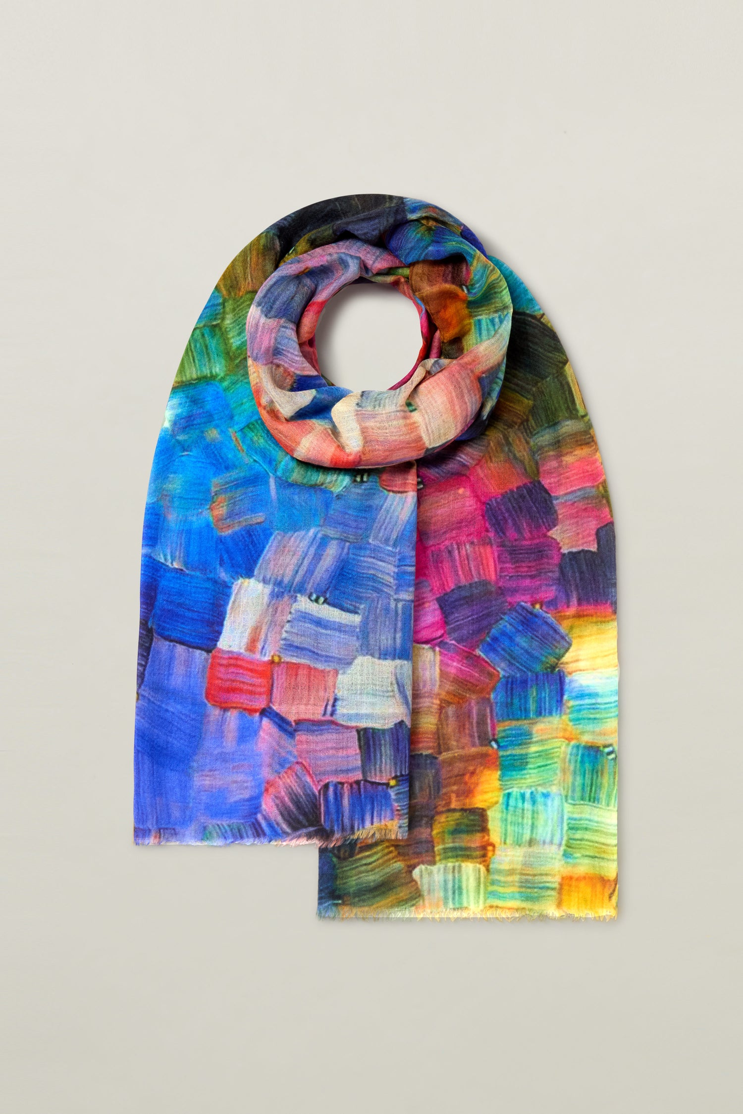 The Painterly Merino Wool Scarf, showcasing a mosaic-like pattern with various shades of blue, pink, green, yellow, and orange, is displayed against a plain background.