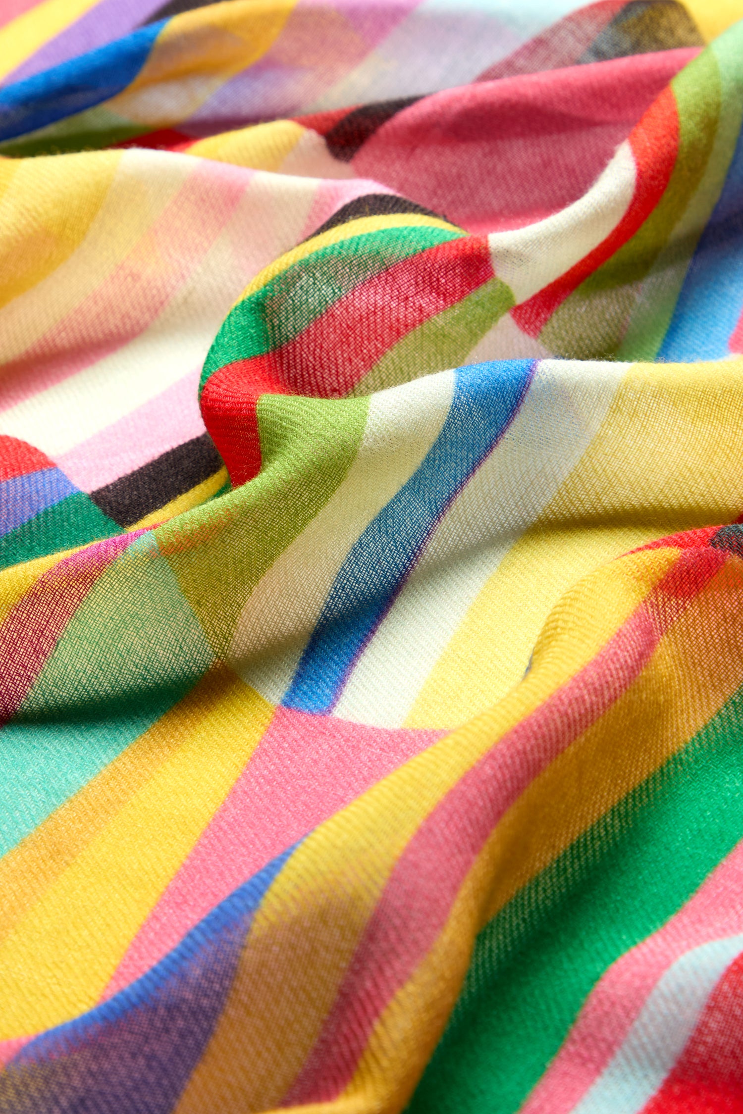 A close-up of the Geometric Rainbow Stripe Wool Scarf showcases its vibrant fabric, with stripes in various shades of yellow, red, green, blue, and pink. This high-quality wool scarf features intricate geometric patterns and appears soft and slightly crumpled.