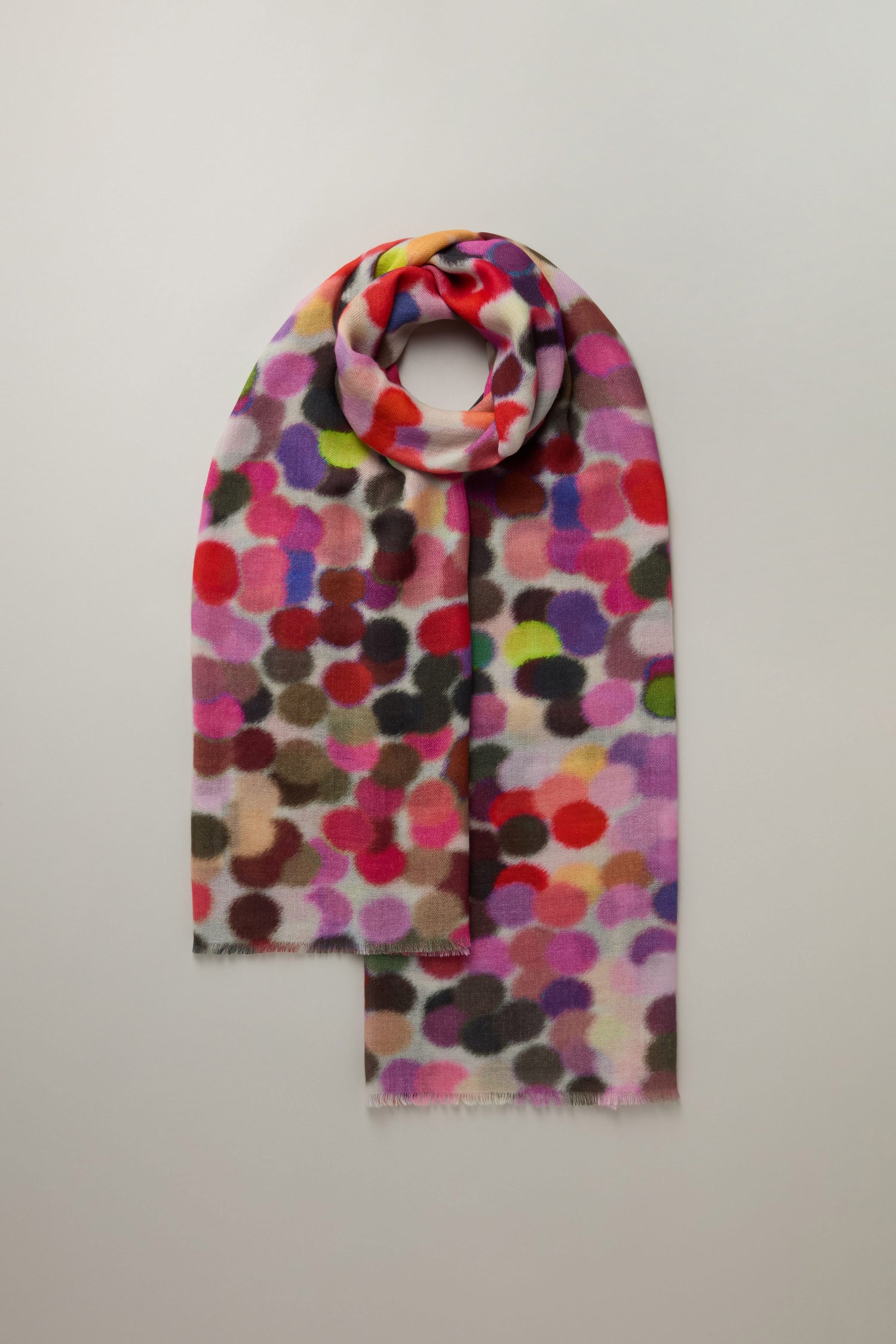 The Dotty About You Scarf Wool Blend features a colorful polka dot pattern with vibrant hues of pink, red, purple, and black. It's elegantly arranged in a circular shape on a white background.