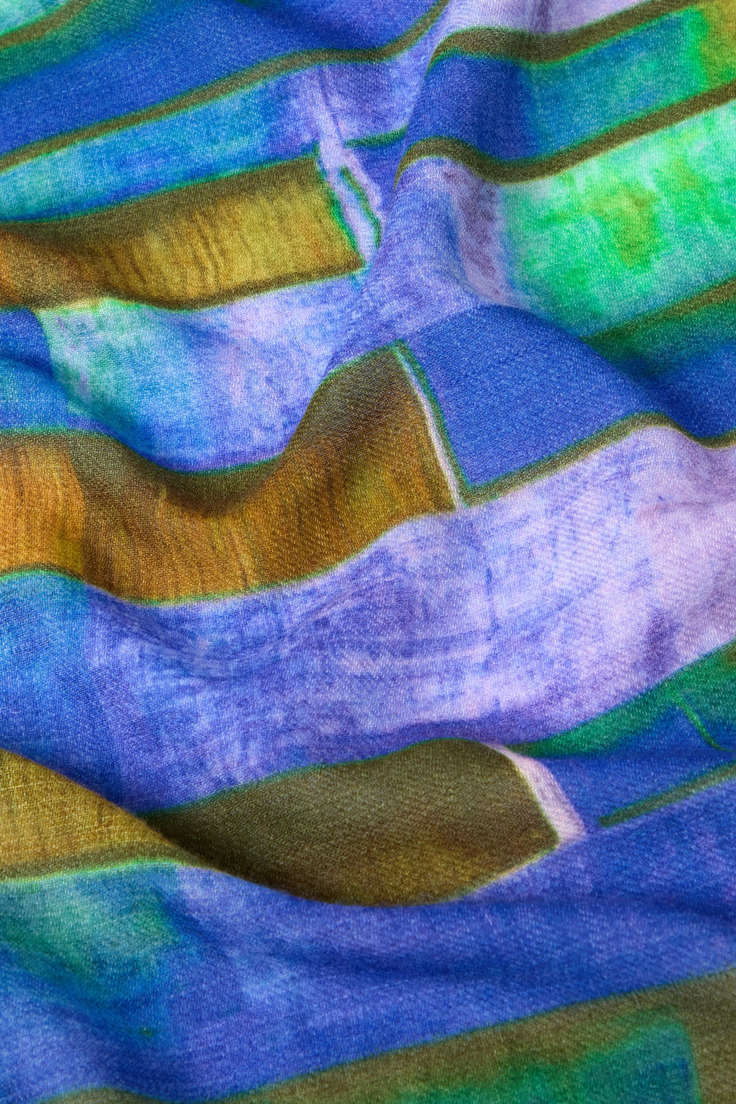 Close-up of the Fragment Wool Scarf showcasing its vibrant fabric with a pattern of horizontal stripes in shades of blue, green, and yellow. The slight texture is visible, and the premium wool scarf appears to be slightly wrinkled. Made in India.