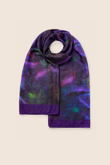 The Cosmos Silk Scarf features dark purple edges and a multicolored, iridescent pattern set against a beige background.