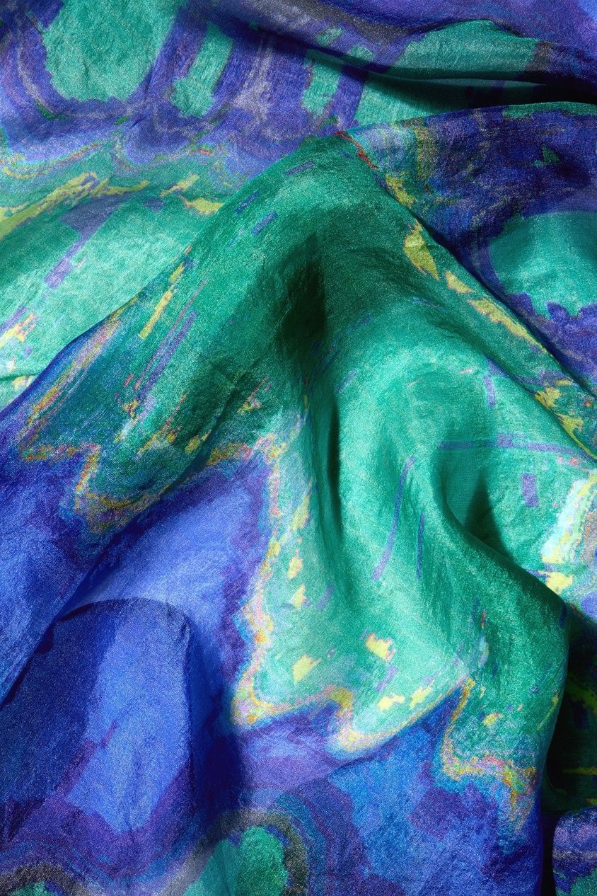 A close-up of an elegant Mineral Silk Scarf reveals its luxurious blue and green wavy fabric with a swirling pattern and glossy texture, reminiscent of the finest silk. Ideal as a luxury accessory, it adds sophistication to any outfit.