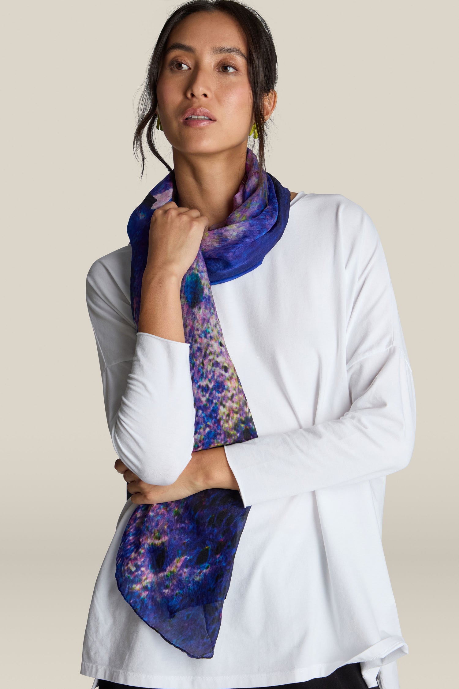 A person wears a white long-sleeve top and a Quartz Silk Scarf. They have dark hair tied back and are looking slightly to the side.