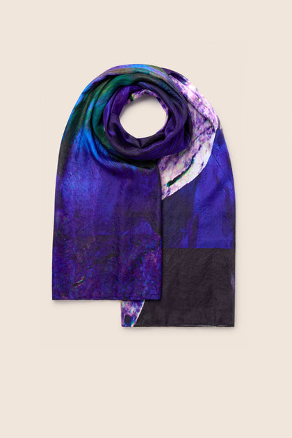 The Quartz Silk Scarf, with its folded, colorful design featuring shades of purple, blue, green, and hints of white on a plain background reminiscent of quartz crystal formations, brings an elegant touch to any outfit.