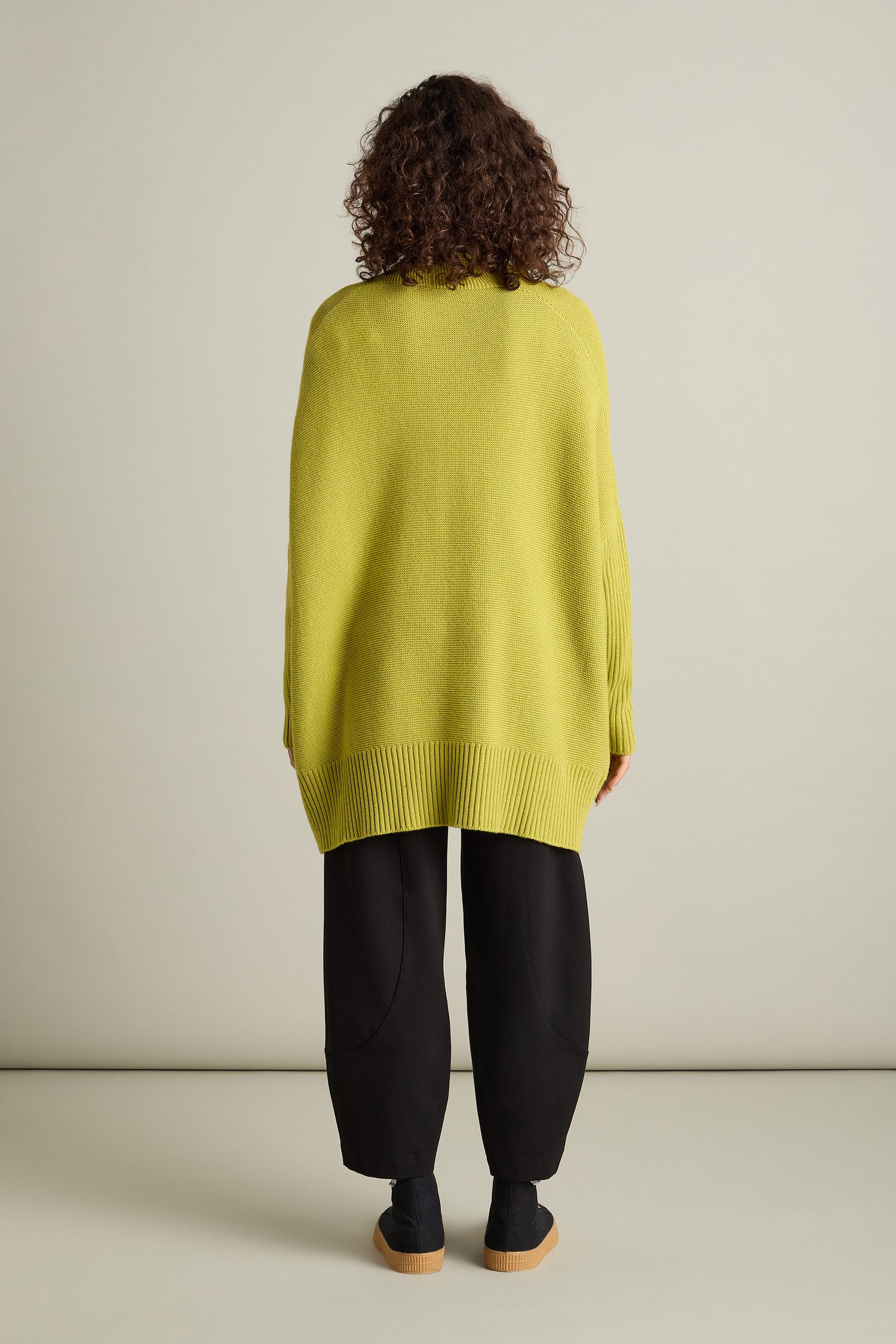 A person with curly hair is wearing a Pocket Detail Rib Cardi in yellow and black pants, standing with their back to the camera against a plain background.