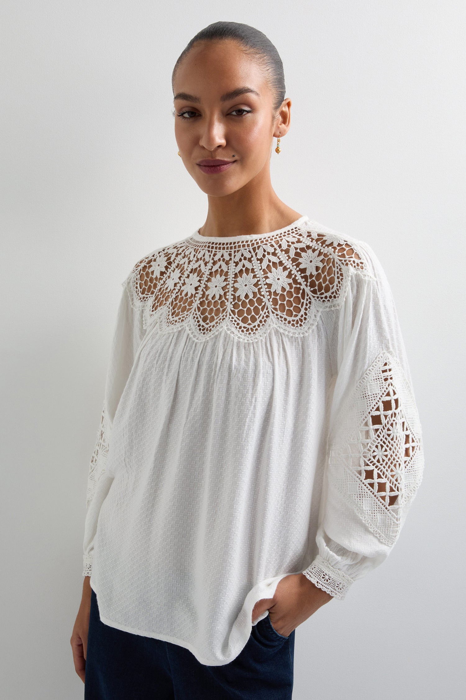 Elegantly draped in the Floral Lace Trim Top with delicate lace on sleeves and neckline, a person stands poised against a plain background, highlighting the timeless style of KNT6038-FLA.