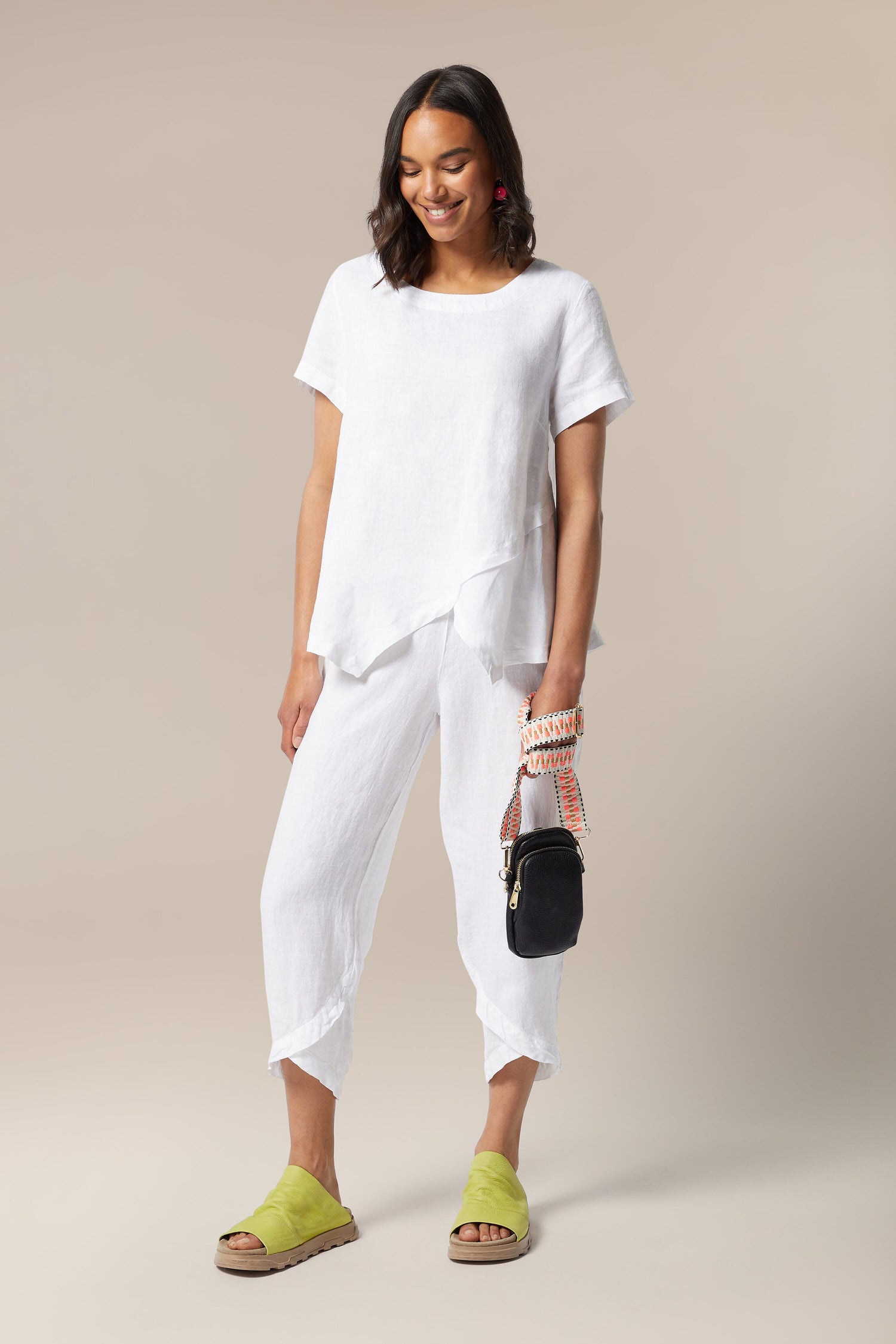 Kris-Ana presents a woman showcasing style-led designs in her ensemble of white linen pants and Mini Crossbody Bag.