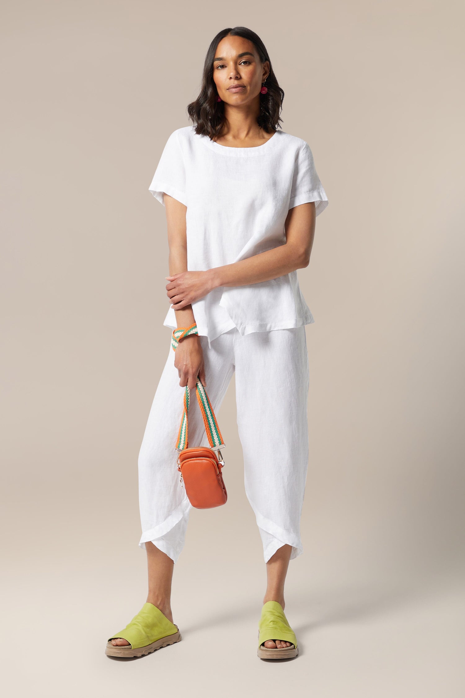 The model is wearing white linen pants and an orange Mini Crossbody Bag.