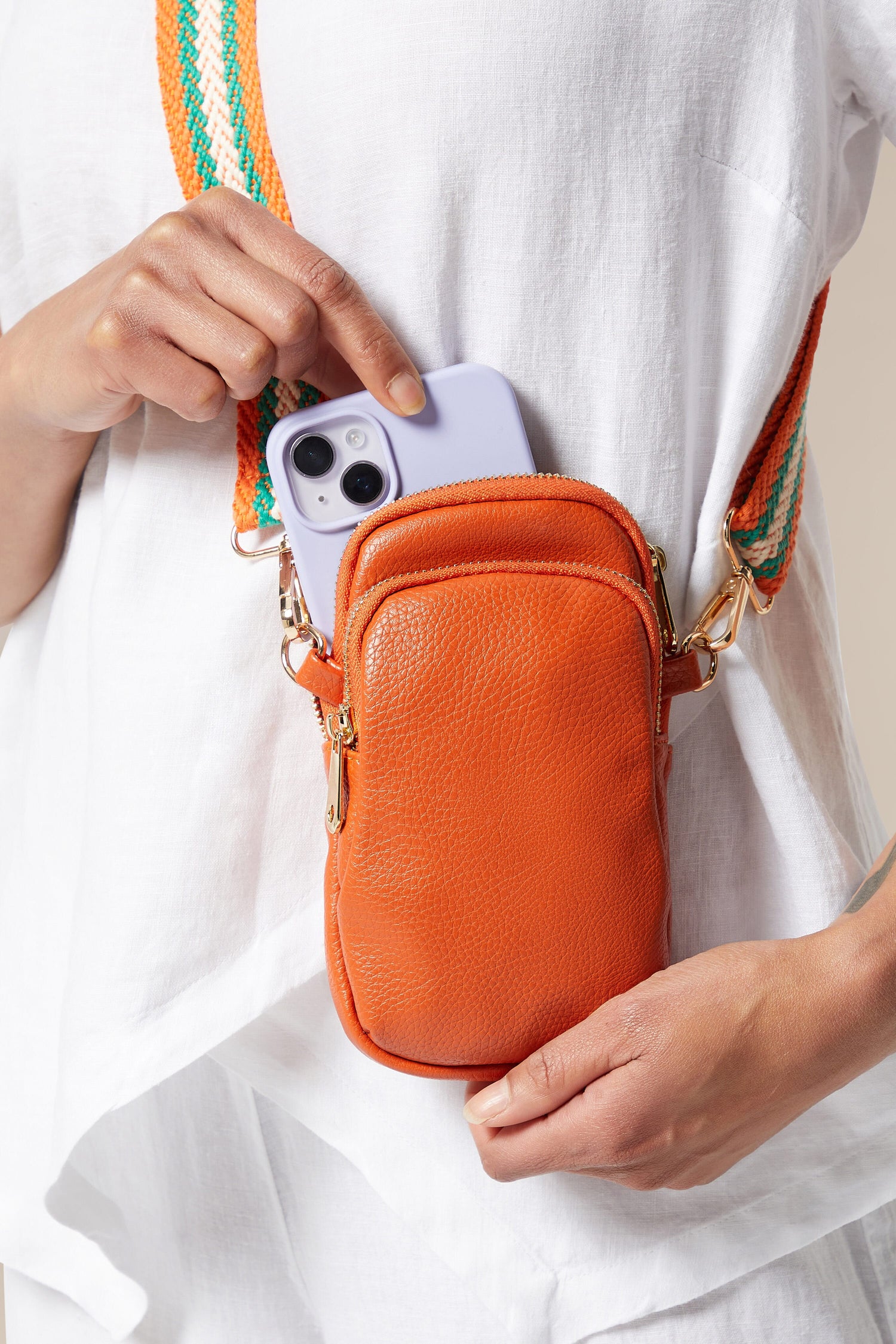 A woman clutching a stylish orange Mini Crossbody Bag.