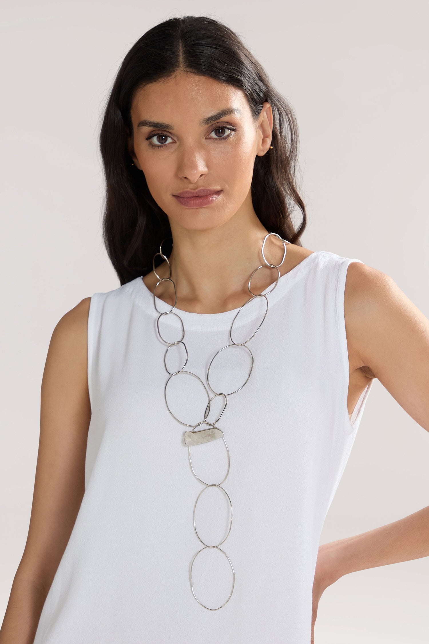 A woman with long, dark hair is wearing a sleeveless white top and the Handmade Crystal Quartz Rings Necklace. She stands against a plain, light background.