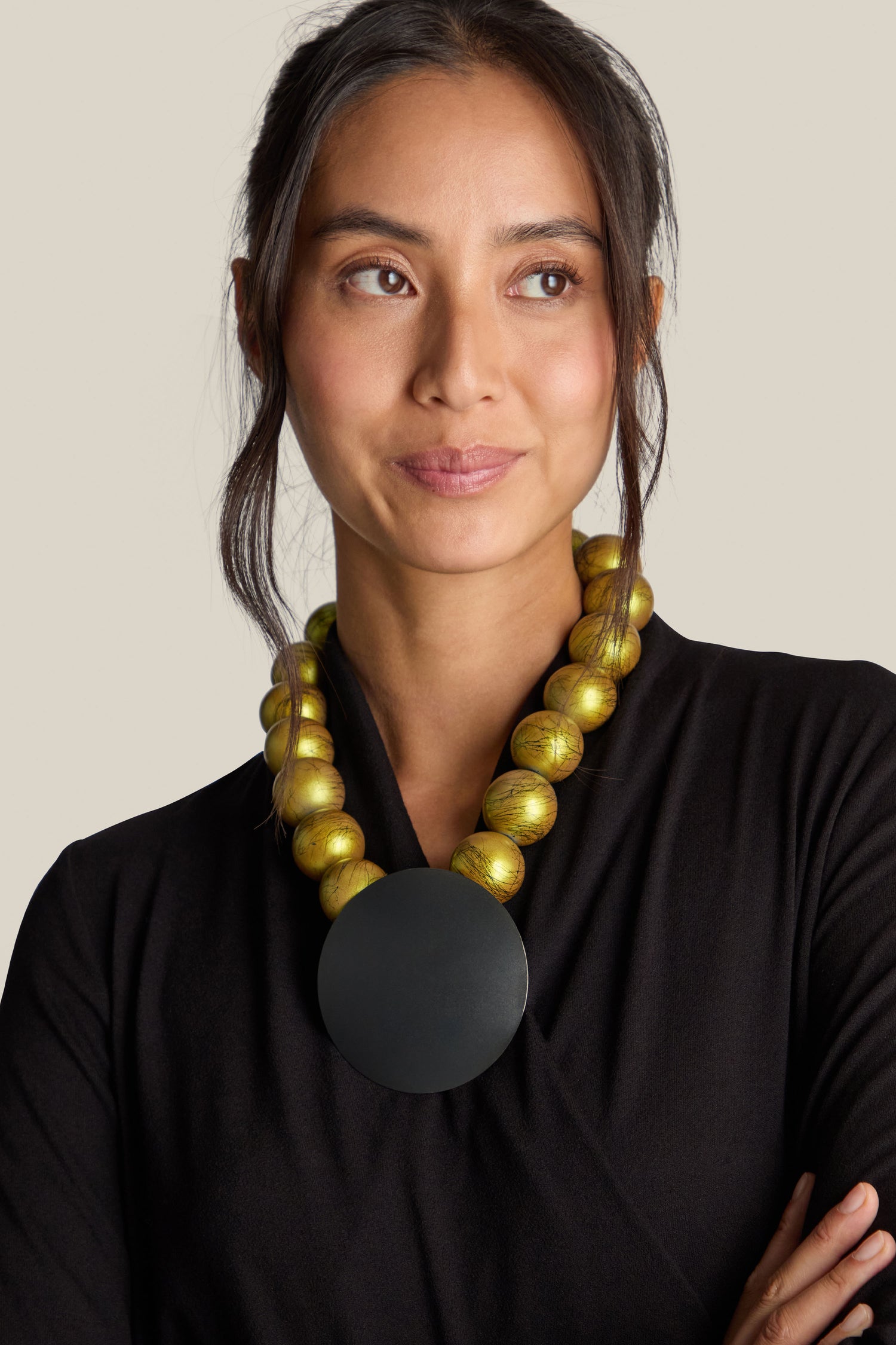 A person with long hair, wearing a black top and the Handmade Eclipse Necklace featuring a chunky beaded design with a large round pendant that has a contemporary edge, is looking to the side.