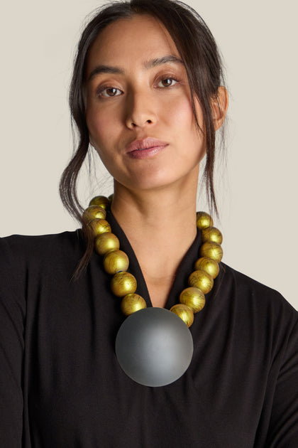 Woman wearing the Handmade Eclipse Necklace, adorned with a bold round pendant, dressed in a black top, posing against a plain background.