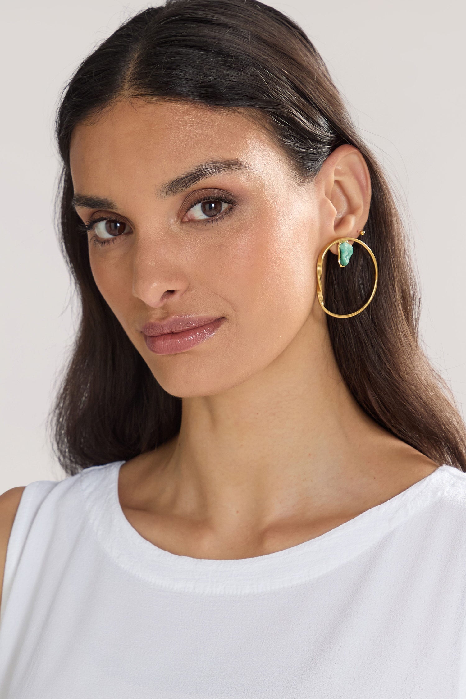 A woman with long dark hair, wearing a white sleeveless top and showcasing the Handmade Agate Hoop Earrings, gazes at the camera with a neutral expression.