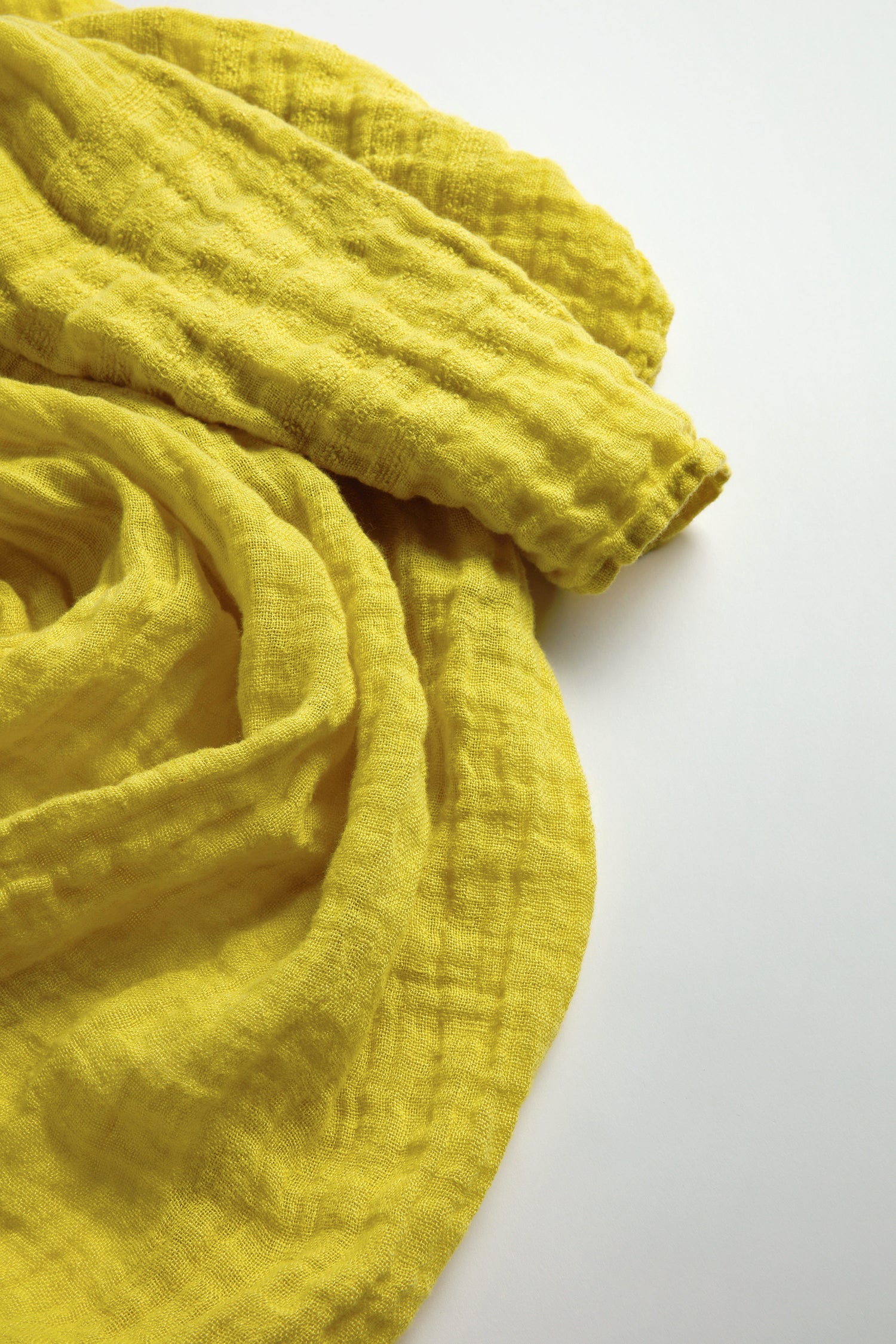 A crumpled, textured yellow fabric similar to a Crinkle Linen Scarf is elegantly draped over a light-colored surface.