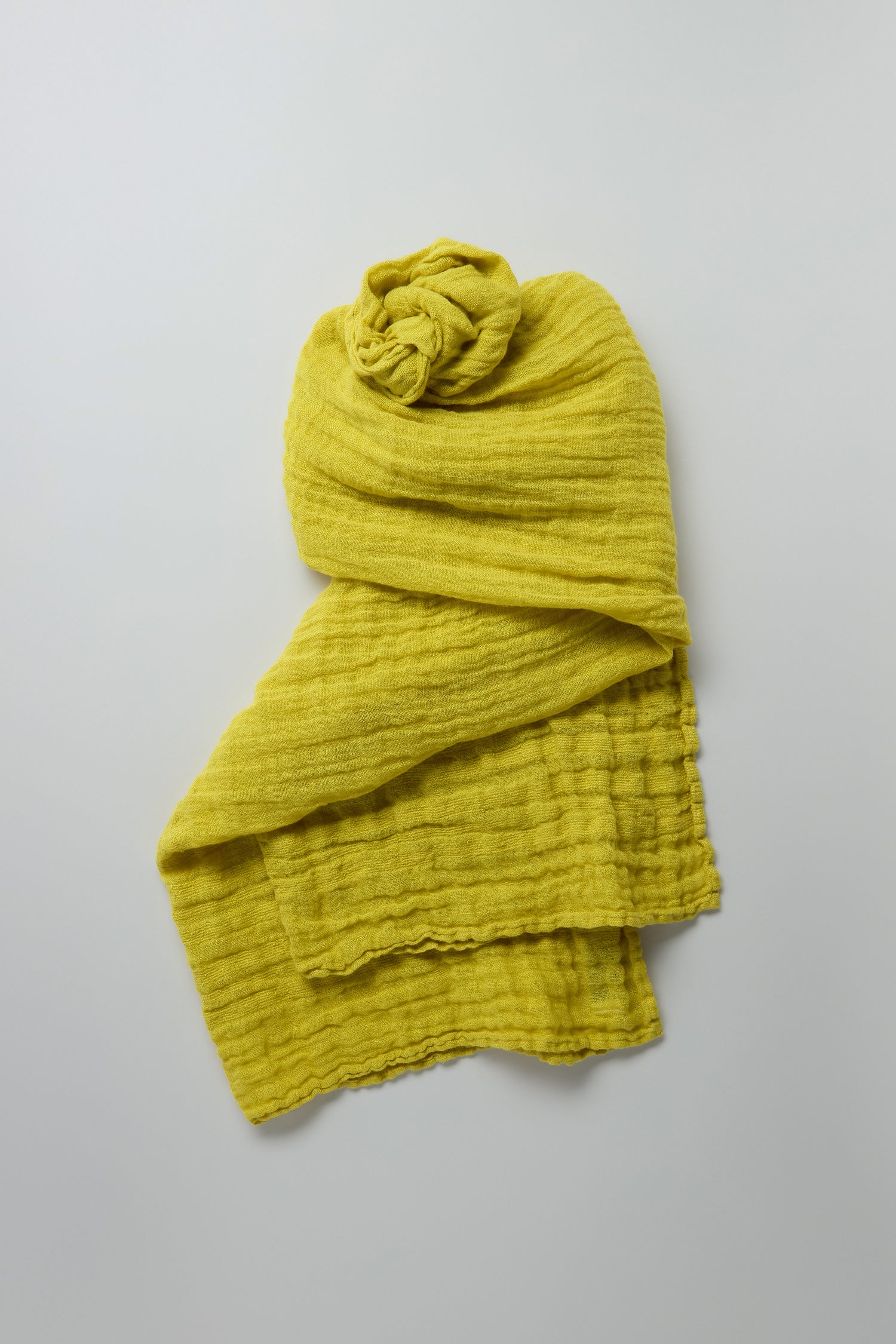 A lime-green Crinkle Linen Scarf sits gracefully on a neutral gray backdrop, highlighting its lightweight charm.