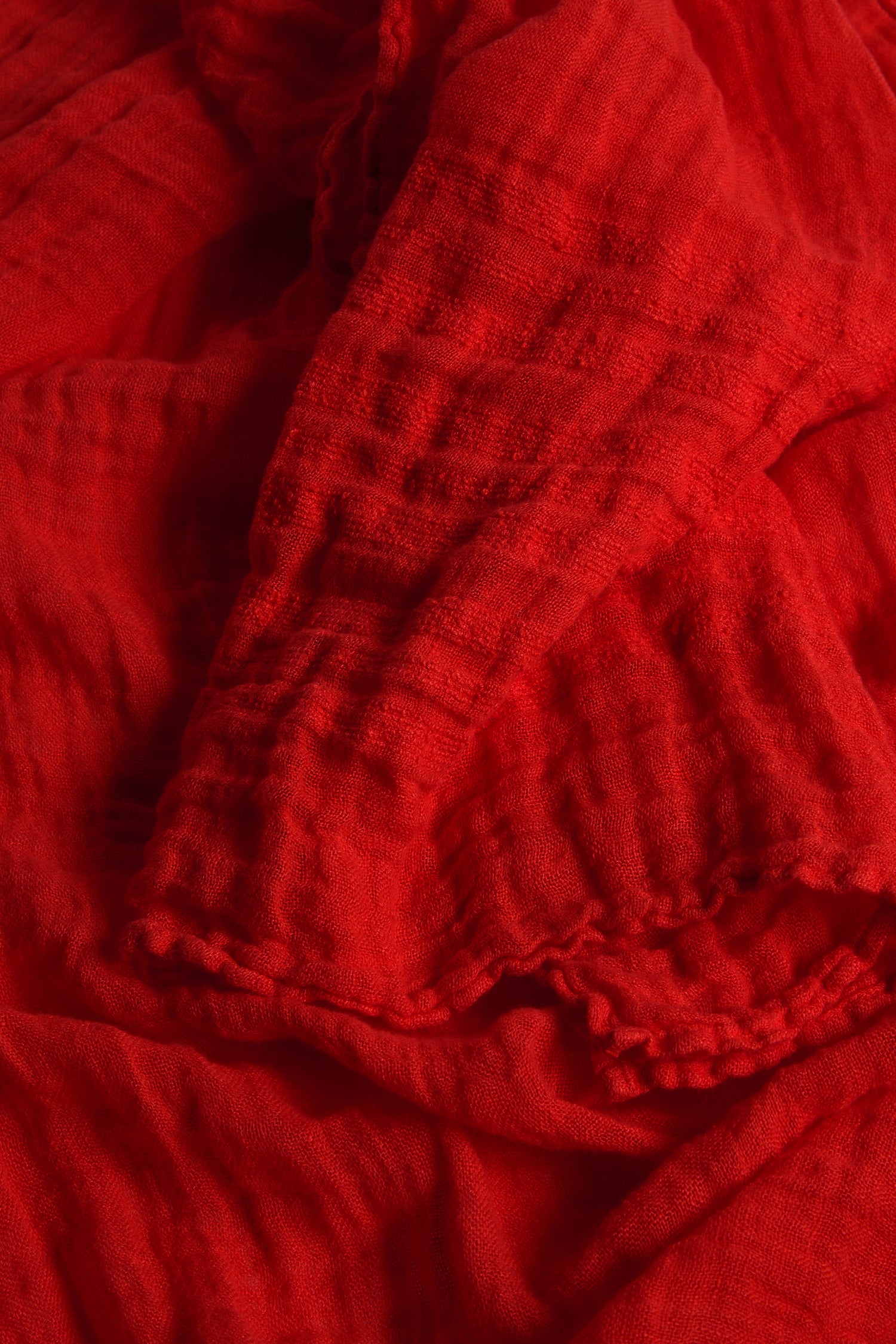 A detailed view of the crumpled, textured red fabric with visible folds and shadows evokes the luxurious feel of a Crinkle Linen Scarf—an ideal, lightweight accessory for seasonal dressing.