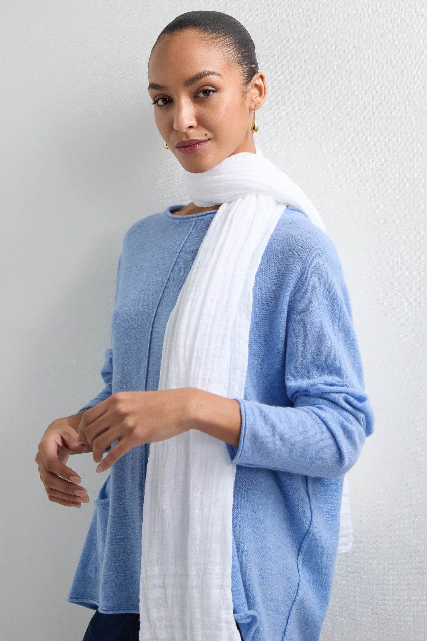 Against a plain background, a person wearing a blue sweater is styled with a Crinkle Linen Scarf, showcasing its lightweight, crinkled texture.