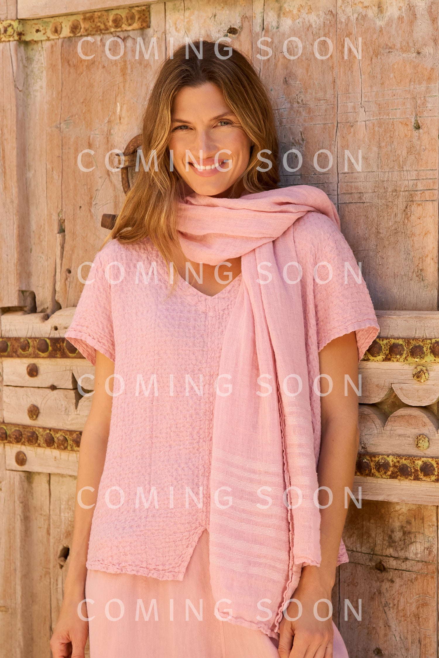 A woman in a light pink top, Crinkle Linen Scarf, and skirt stands before a wooden door. "COMING SOON" is displayed over the image.