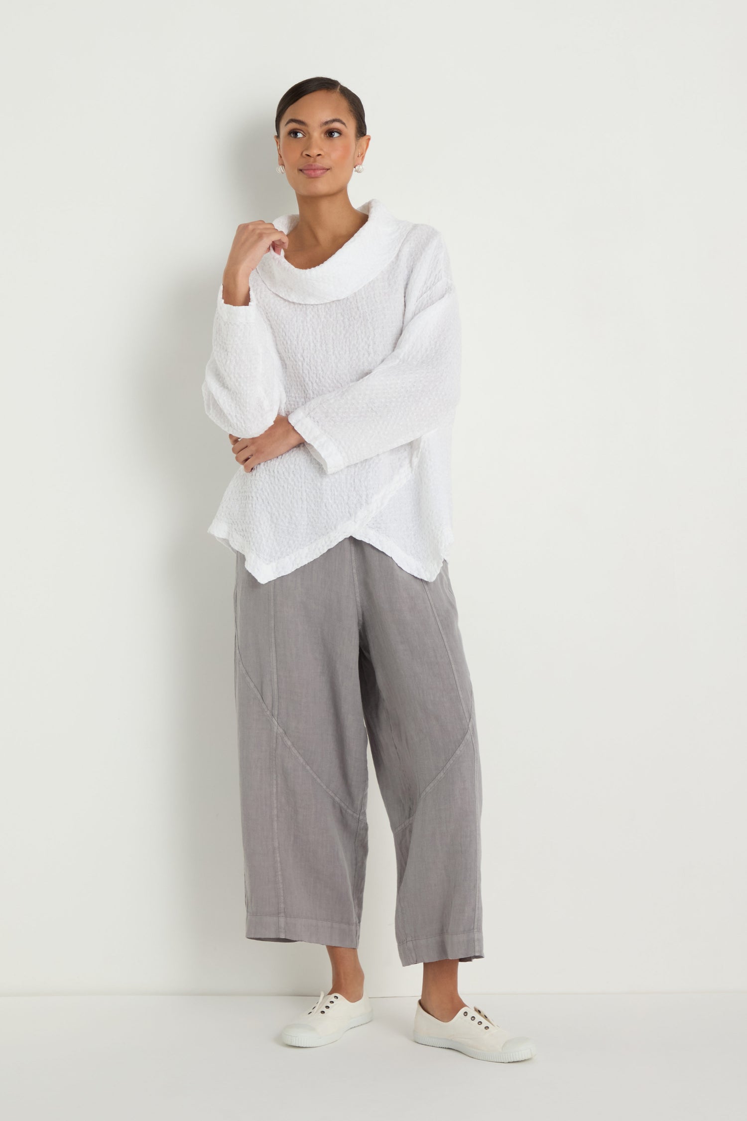 Person standing against a white wall, wearing the Waffle Linen Boxy Cowl Neck Top, light gray wide-leg pants, and white sneakers.