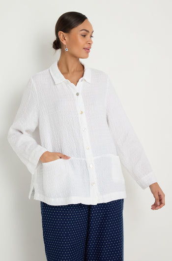 A woman wears the Waffle Linen Pocket Shirt in white with a boxy silhouette and long sleeves, paired with navy blue polka dot pants, standing against a plain light background.