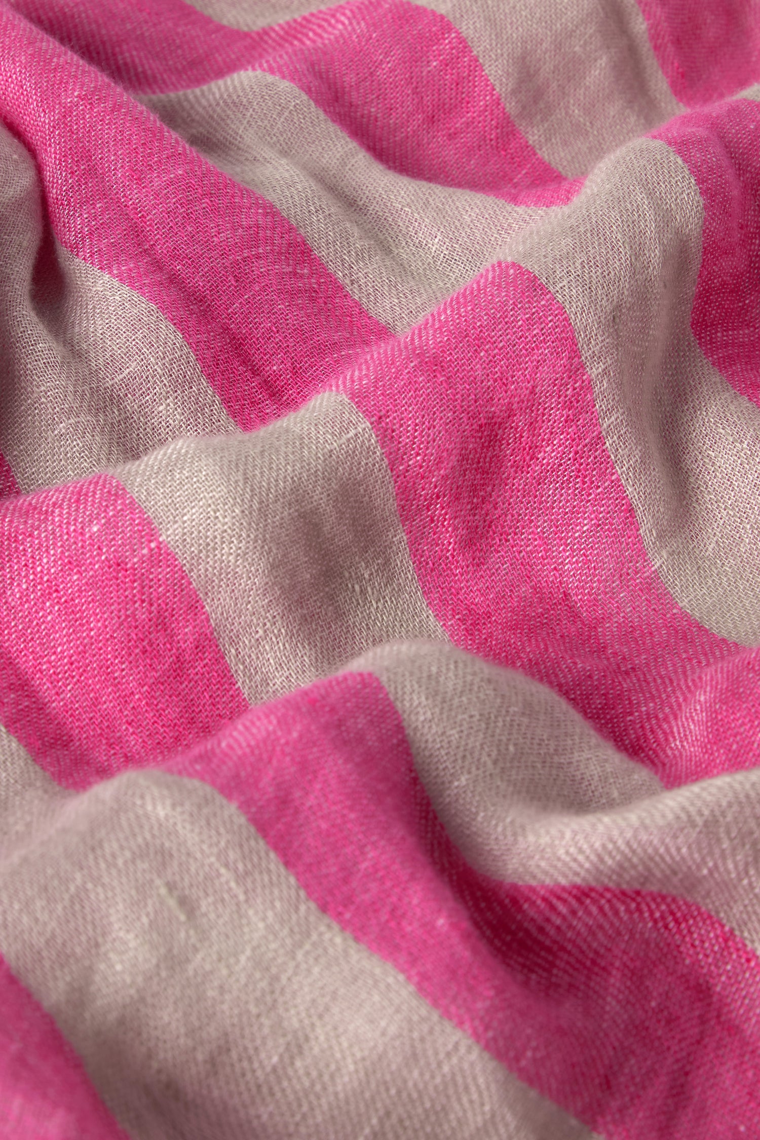 The Linen Stripe Scarf features pink and beige horizontal stripes with a slightly wrinkled texture, making it an elegant accessory for spring or summer outfits.