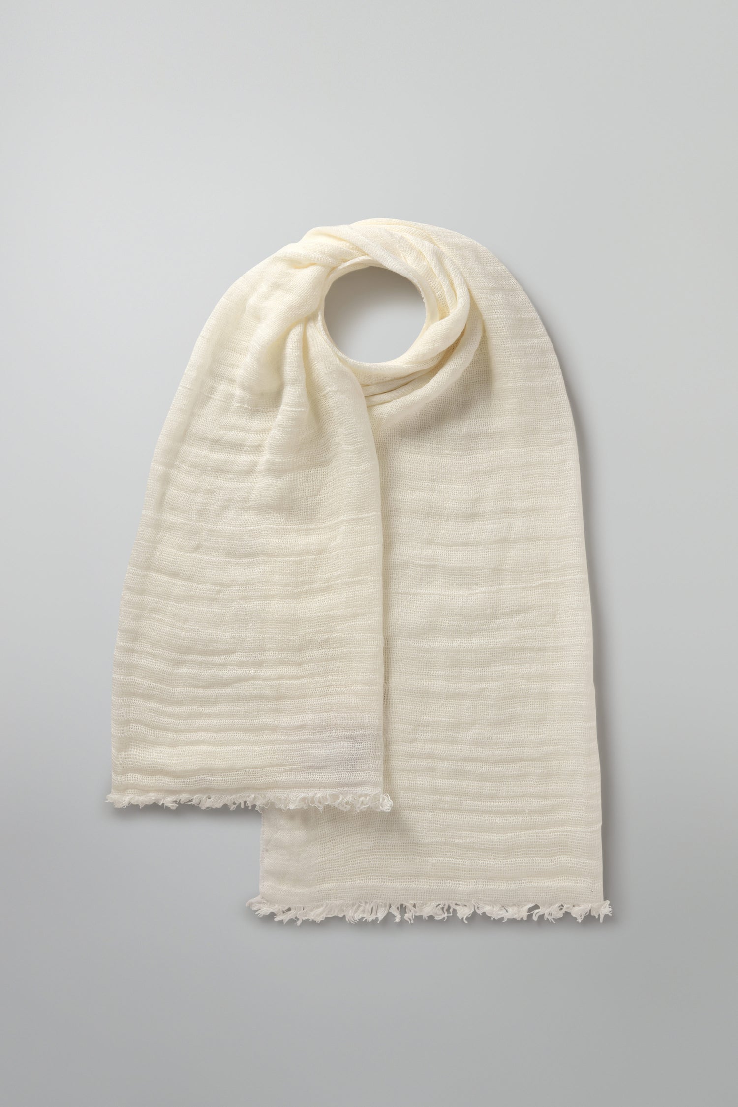 The cream-colored Woven Linen Scarf, crafted from 100% linen and featuring fringed edges, is gracefully displayed on a light gray background.