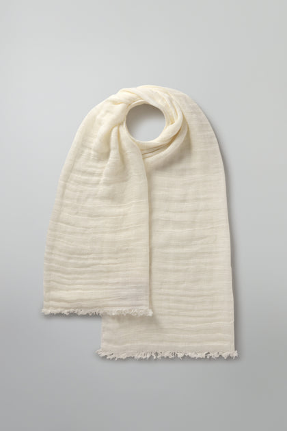 The cream-colored Woven Linen Scarf, crafted from 100% linen and featuring fringed edges, is gracefully displayed on a light gray background.