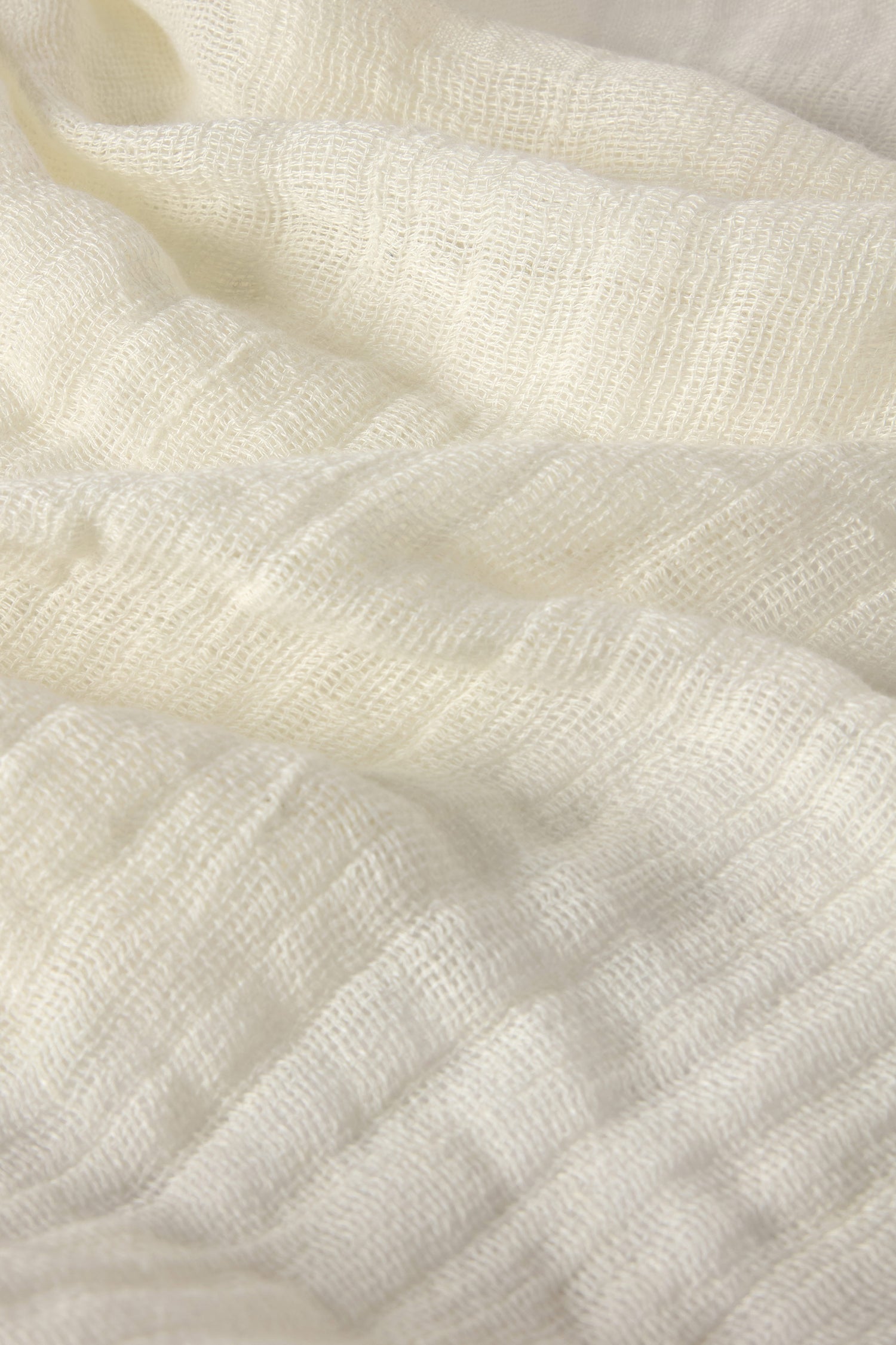 Close-up of the Woven Linen Scarf in soft, white fabric made from 100% linen, featuring a textured surface with gentle folds and a raw-edge finish.