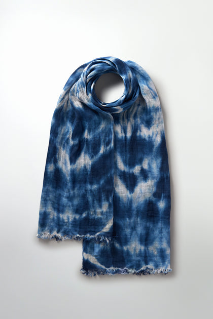 The indigo blue and white Tie Dye Linen Scarf is neatly folded on a plain background, making it an ideal addition to your summer wardrobe.