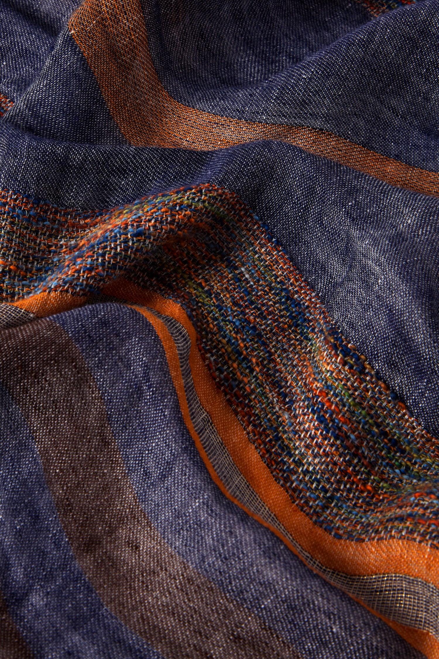 The Denim Detail Linen Stripe Scarf showcases a blend of linen and cotton with blue, orange, and multicolored stripes. Its intricate woven patterns add depth, making it ideal for a spring/summer wardrobe or to enhance any look with its striking denim-inspired detail.