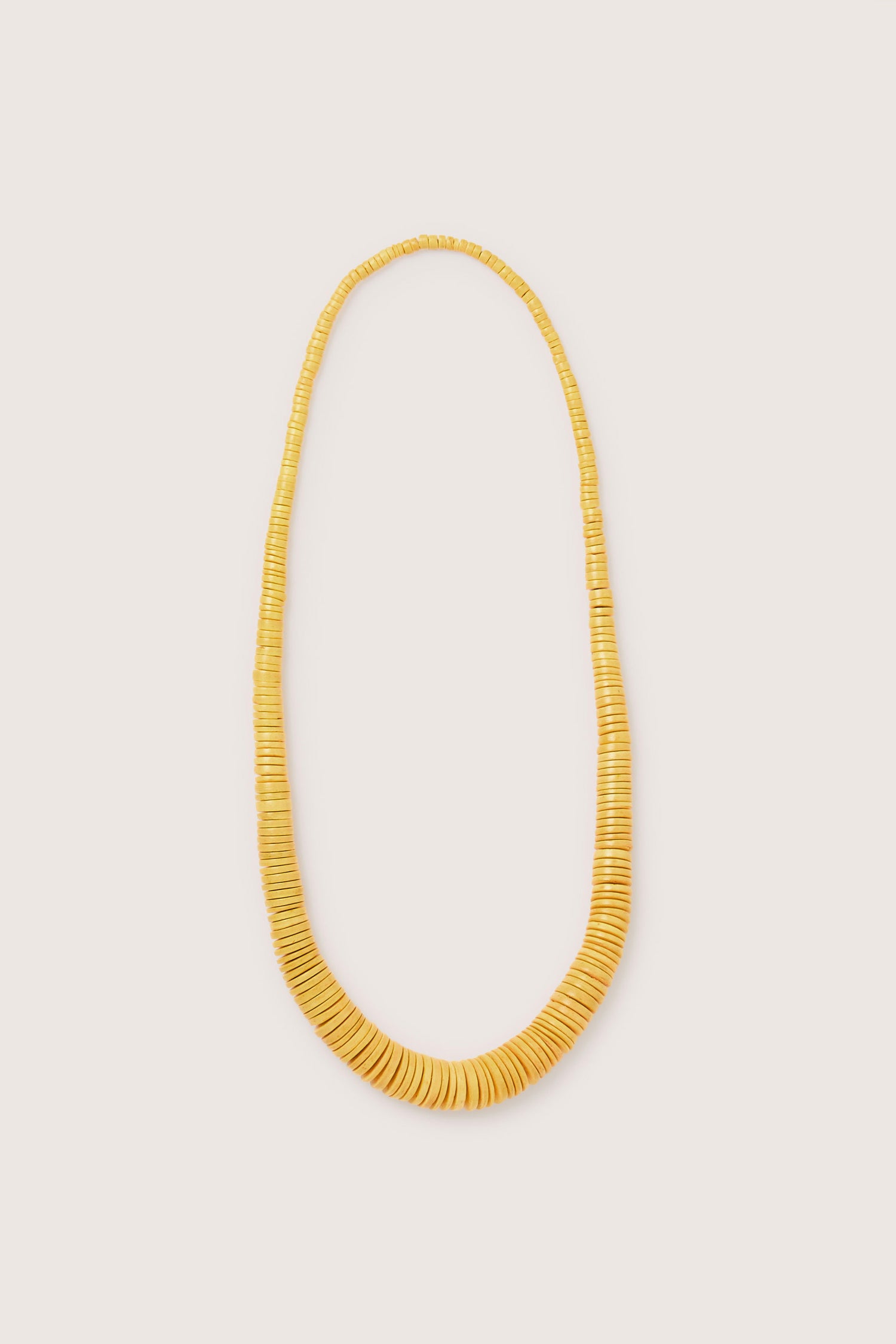 The Long Graduated Coco Disc Necklace, expertly crafted by skilled artisans, showcases uniformly sized round yellow beads meticulously arranged in a continuous strand.