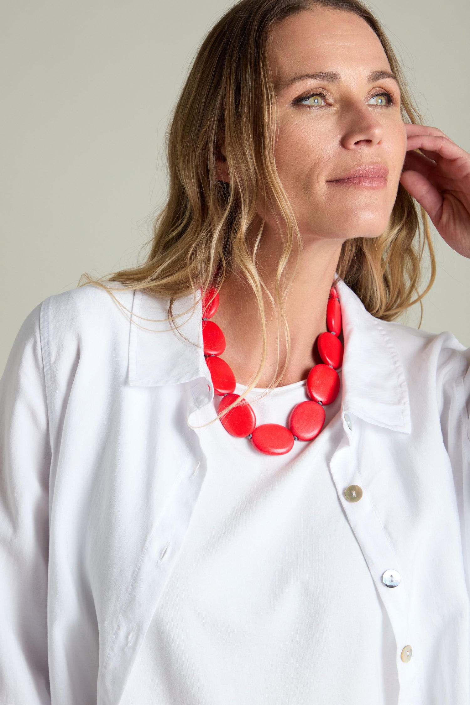 A person with long hair wearing a white shirt and the Short Wooden Pebble Necklace, looking off to the side.