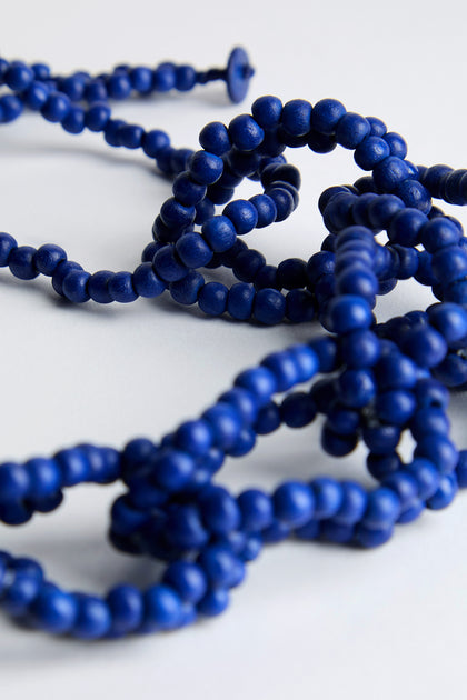 A close-up of the Woven Coco Sphere Necklace's tangled, dark blue strands, crafted from natural coconut beads on a light surface, showcases artisan craftsmanship.