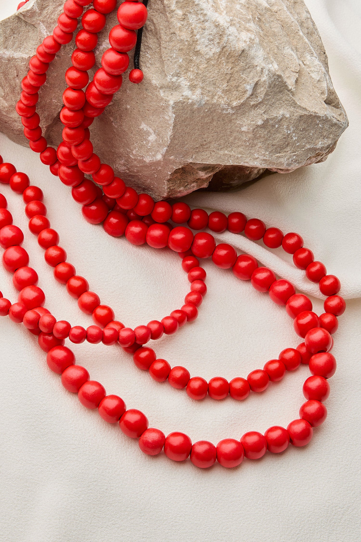 The Wooden Cascade Spheres Necklace is draped over a large rock on a light-colored fabric background, evoking the intricate jewelry craftsmanship found in the Philippines.