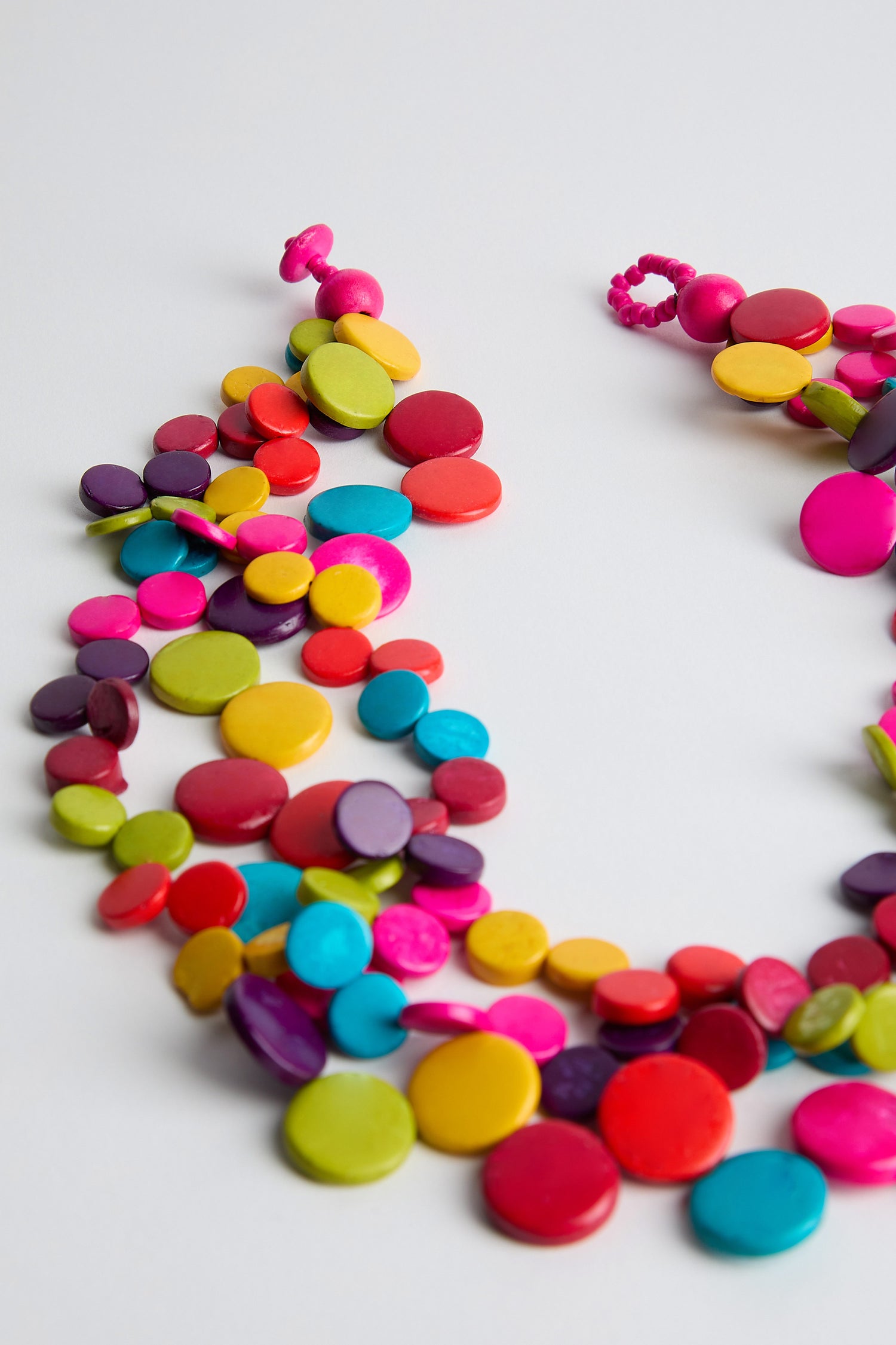 The Rainbow Coconut Cascade Necklace features an array of round, glossy beads crafted from sustainably sourced coconut in red, orange, yellow, green, blue, and pink hues. Set against a plain white background.