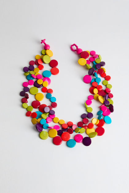 The Rainbow Coconut Cascade Necklace boasts a lively multi-strand design with circular red, yellow, green, blue, purple, and orange beads. Made from sustainably sourced coconut materials, this necklace offers bold layers of color for a striking look.