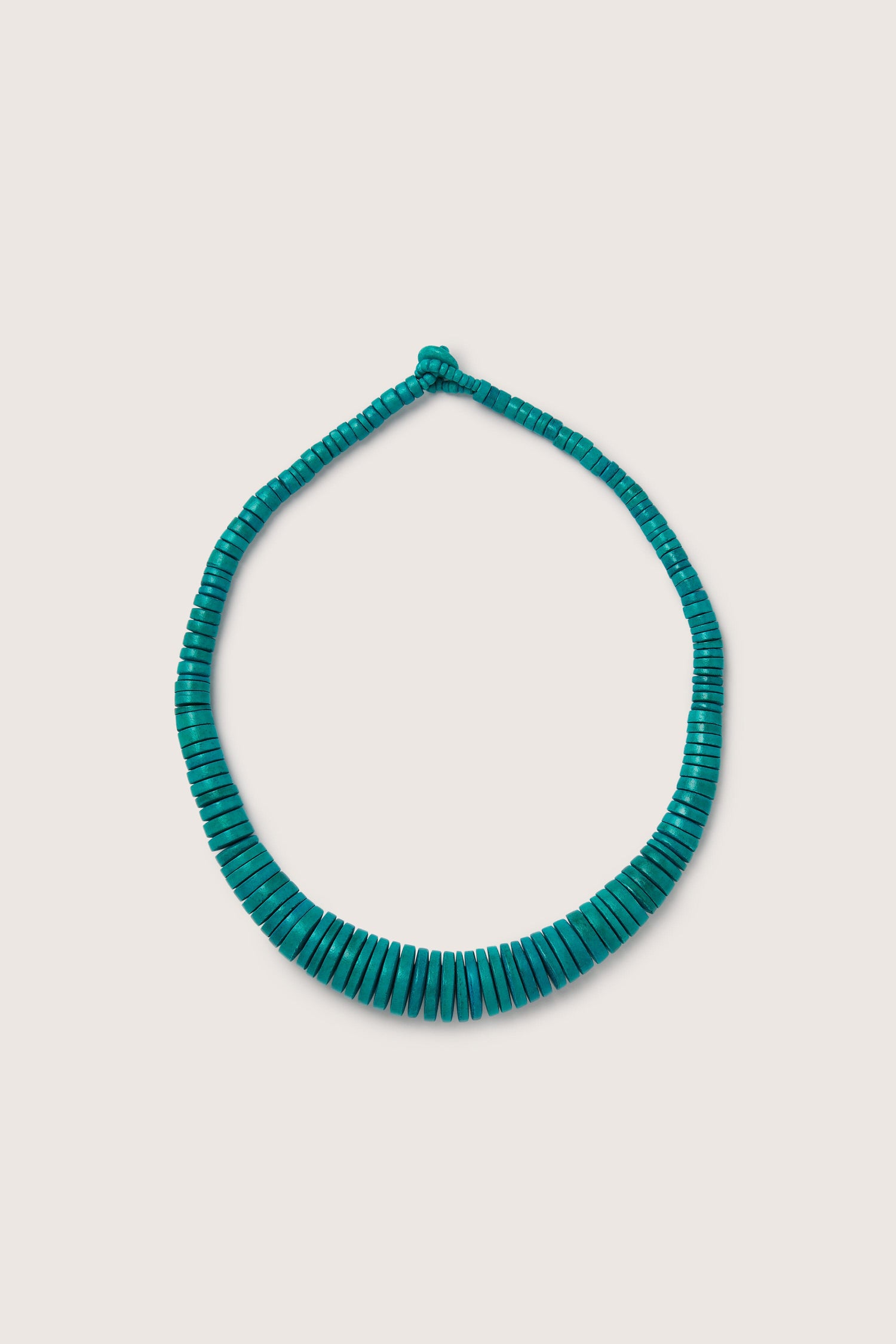 A Graduated Coco Disc Necklace with a bold hue is displayed on a beige background.