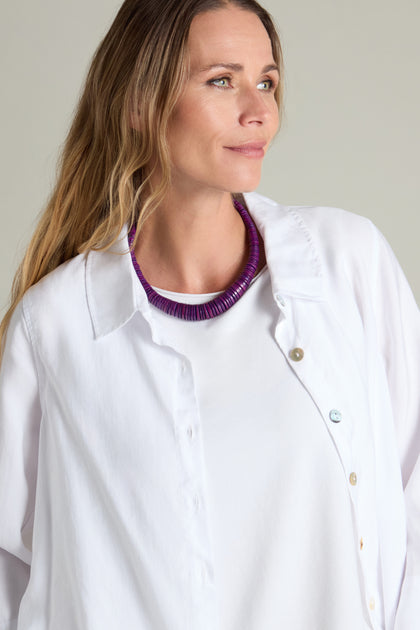 A person with long hair wearing a white shirt and the Short Graduated Coco Disc Necklace from Lotusfeet, looking off to the side against a plain background.