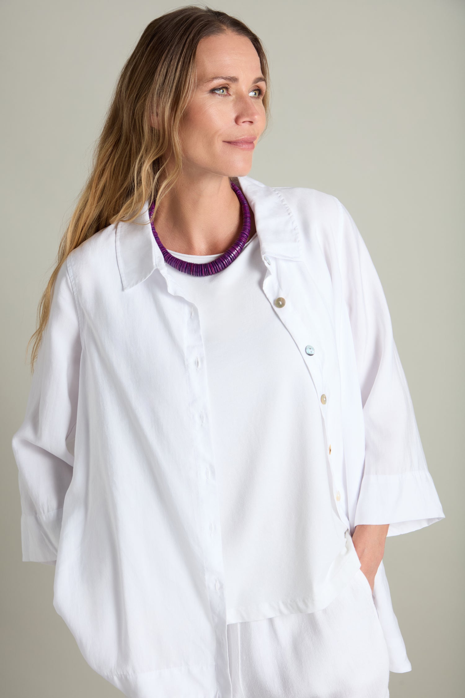 A woman with long hair, dressed in a white button-up shirt over a white top, stands against a plain background, accessorized with the Short Graduated Coco Disc Necklace.