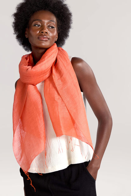 A person wearing a white sleeveless top, black pants, and a luxurious **Soft Linen Scarf** in vibrant orange stands against a neutral background.