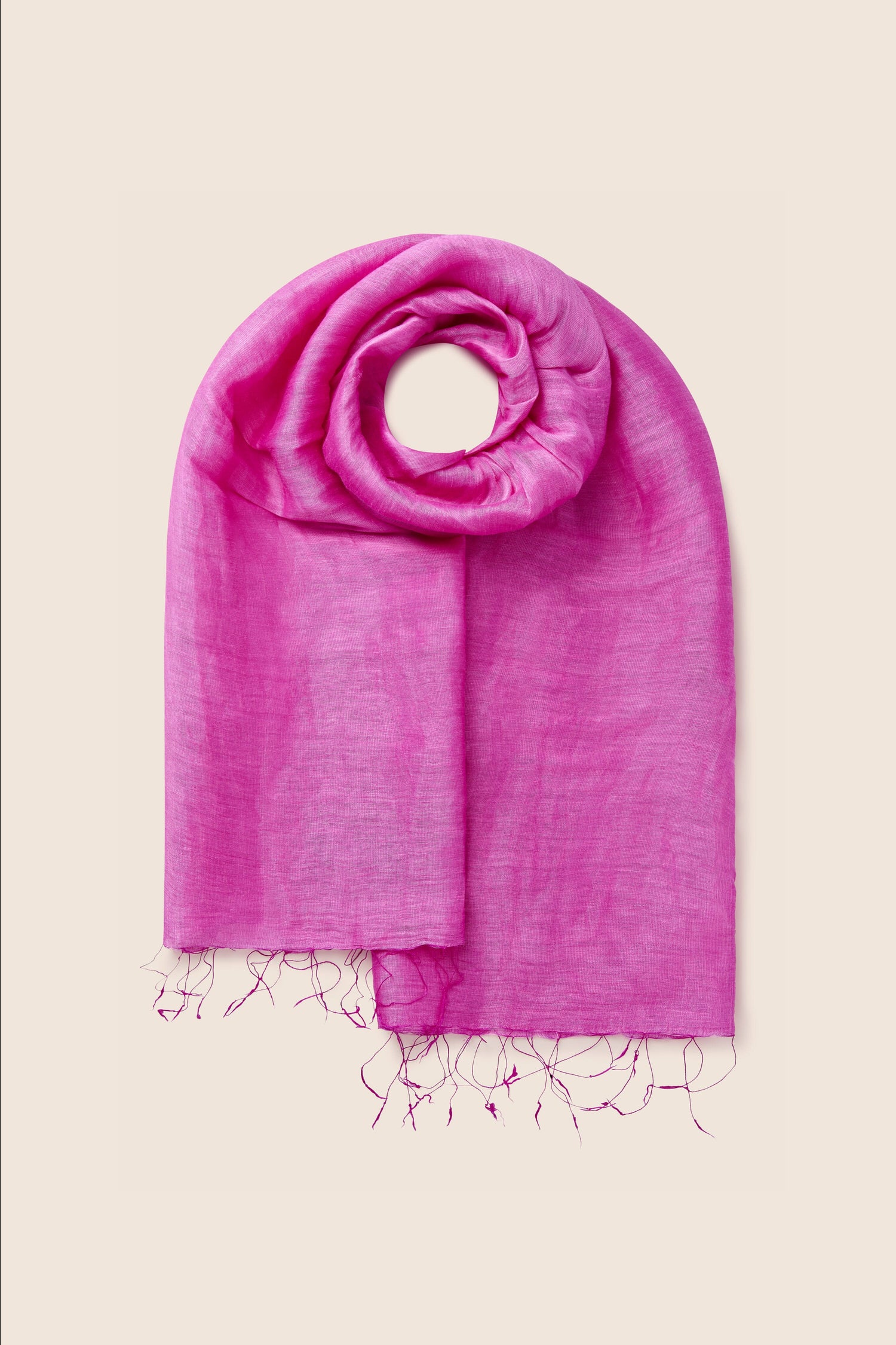 The "Soft Linen Scarf," featuring a bright pink color and made from soft linen, showcases a lightweight design with neatly folded frayed edges against a beige background.