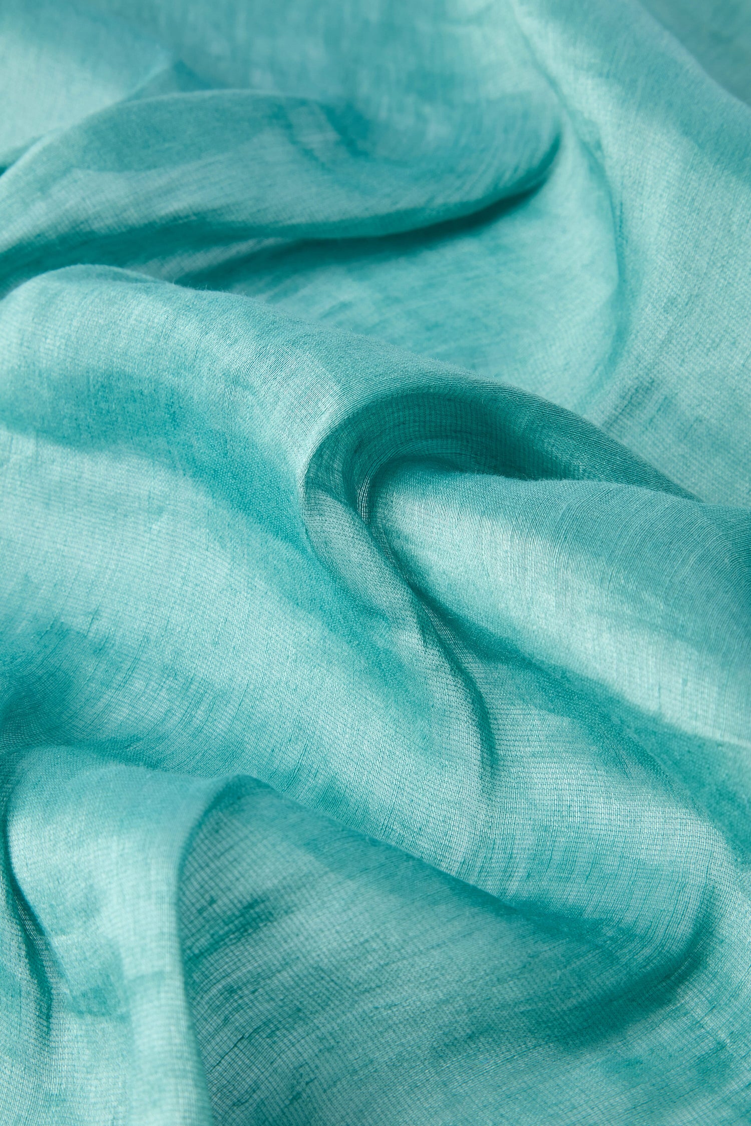 Close-up of a light turquoise, fair trade Soft Linen Scarf featuring smooth folds and a slightly sheer texture.