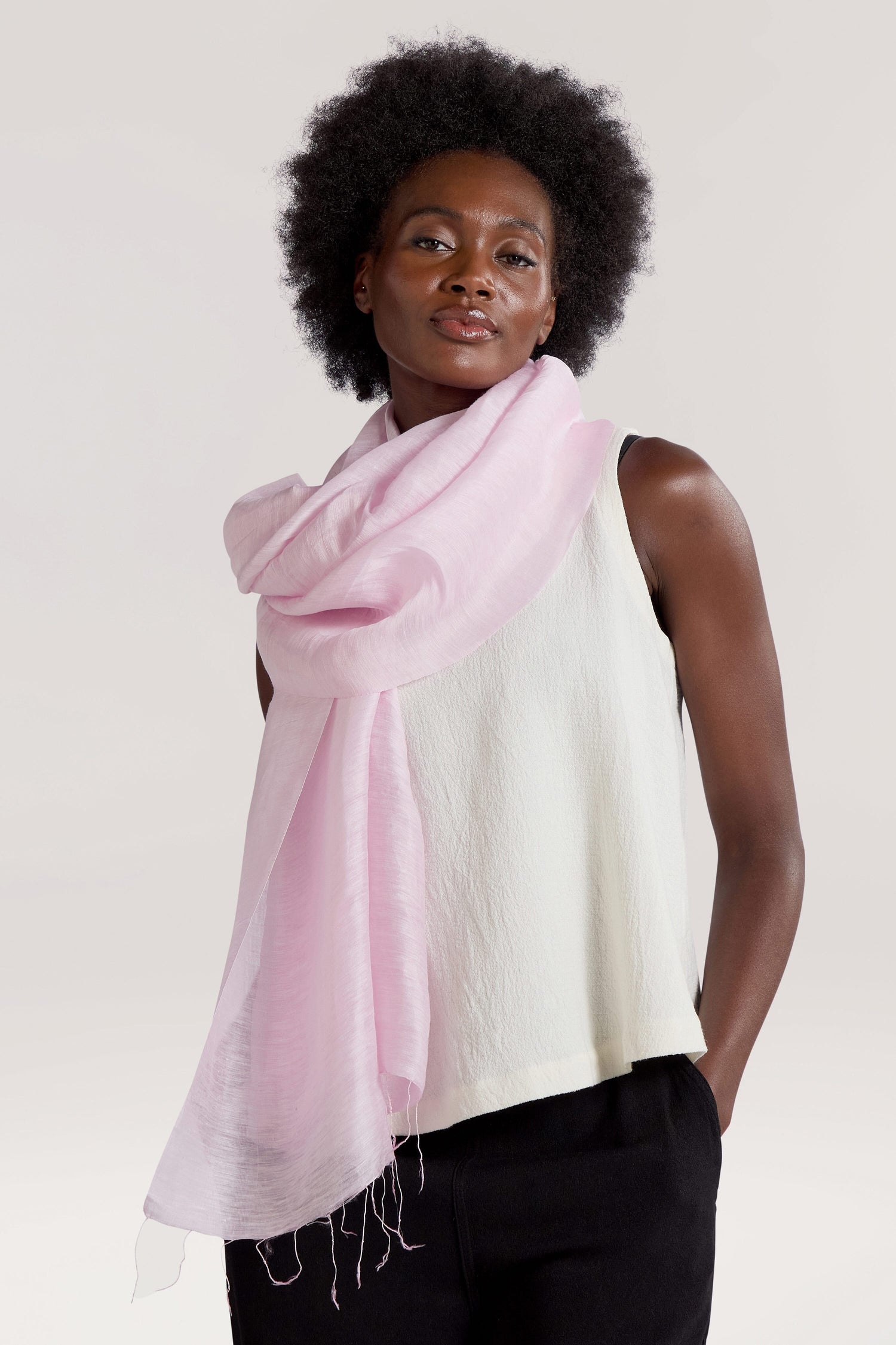 A person with dark curly hair is wearing a sleeveless white top and a Soft Linen Scarf in pink, standing against a plain background.