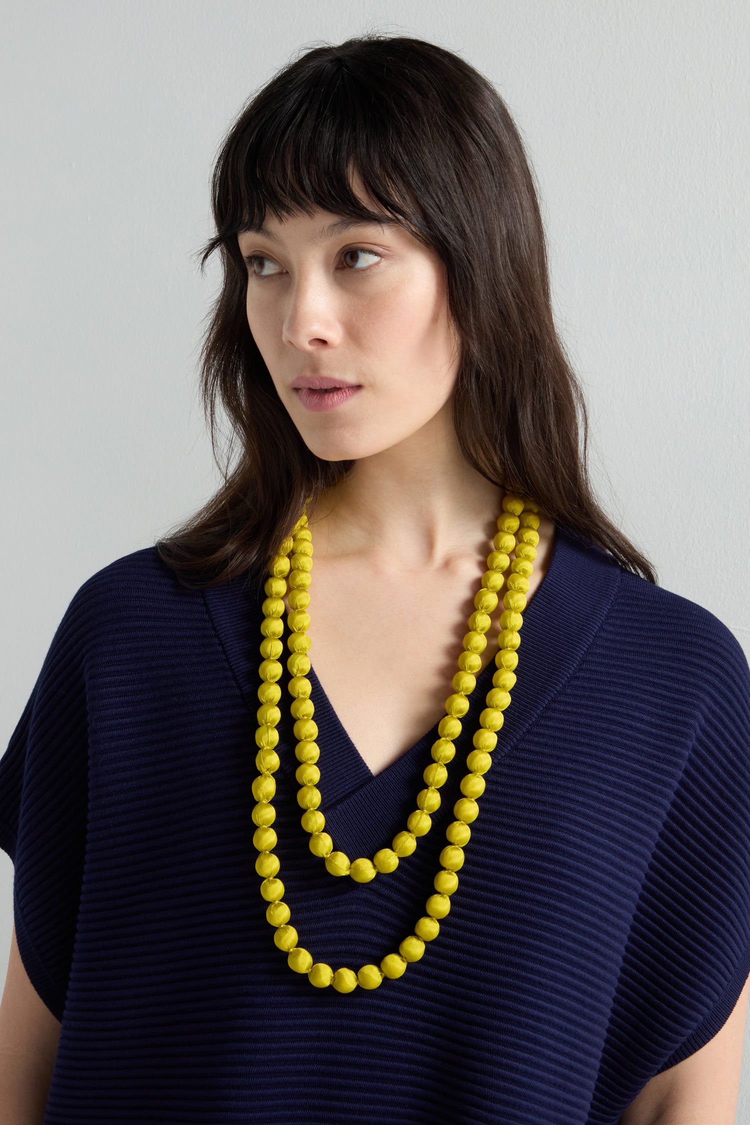 A person in a navy blue sweater stands against a light gray background, showcasing the Handmade Long Silk Spheres Necklace, highlighting artisanal craftsmanship.