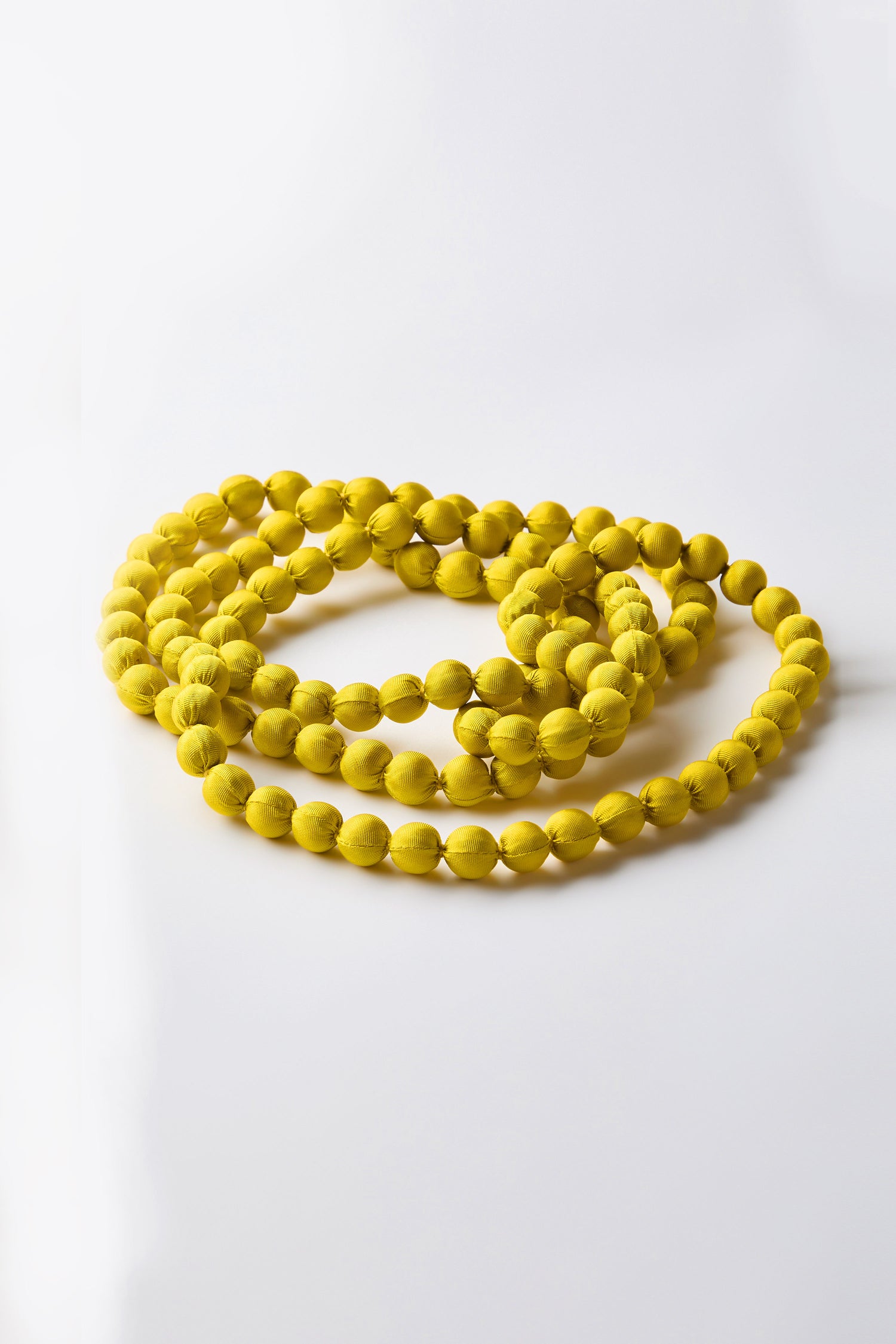 The Handmade Long Silk Spheres Necklace, featuring vibrant yellow beads, coils gracefully on a white surface.