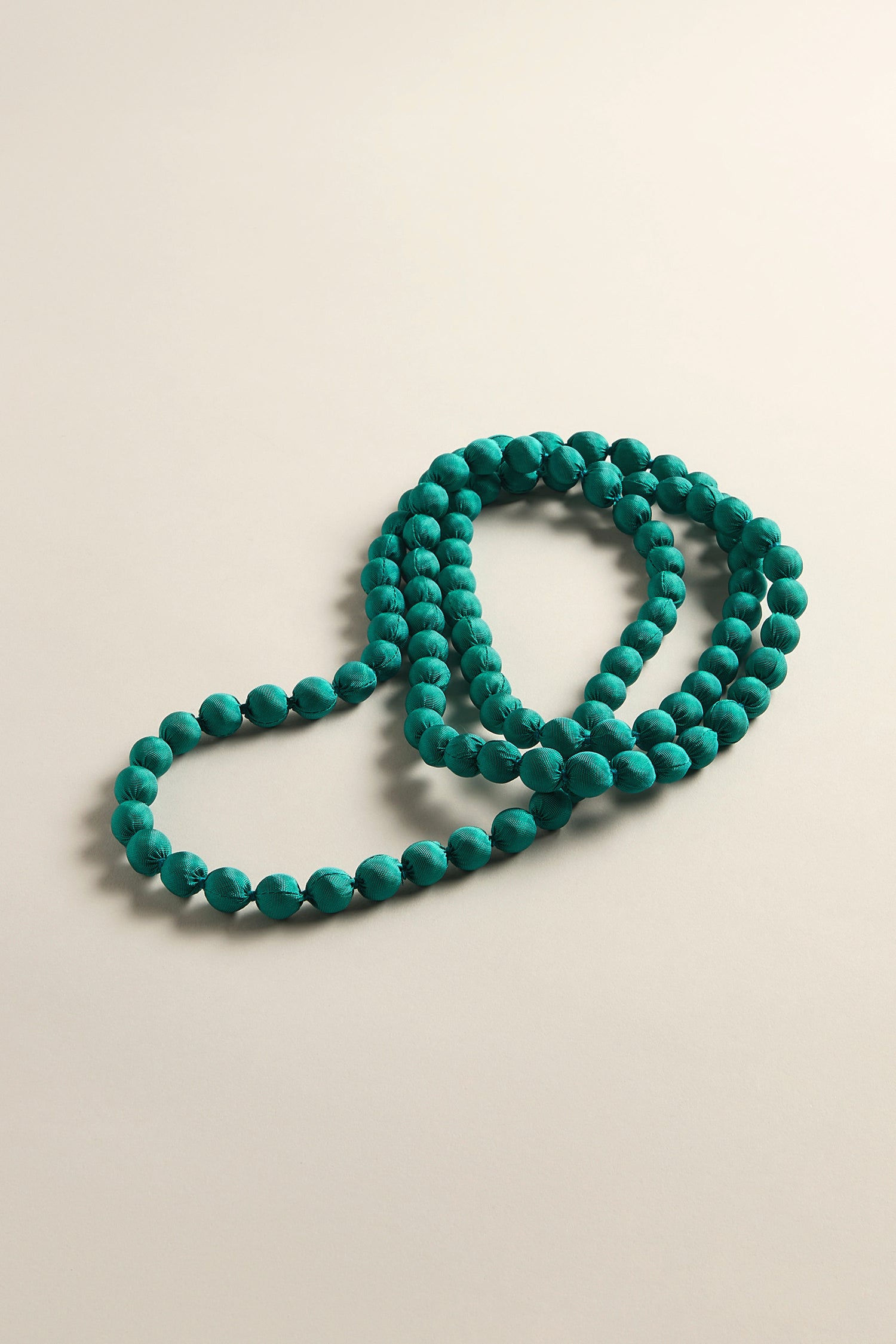 A Handmade Long Silk Spheres Necklace, highlighting artisanal craftsmanship with turquoise beads, is elegantly coiled on a neutral background.