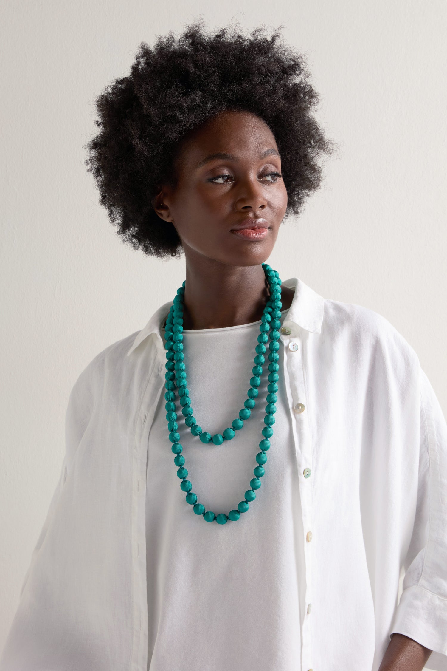 A person wearing a white shirt showcases vibrant accessories, including a Handmade Long Silk Spheres Necklace that highlights artisanal craftsmanship against a plain background.