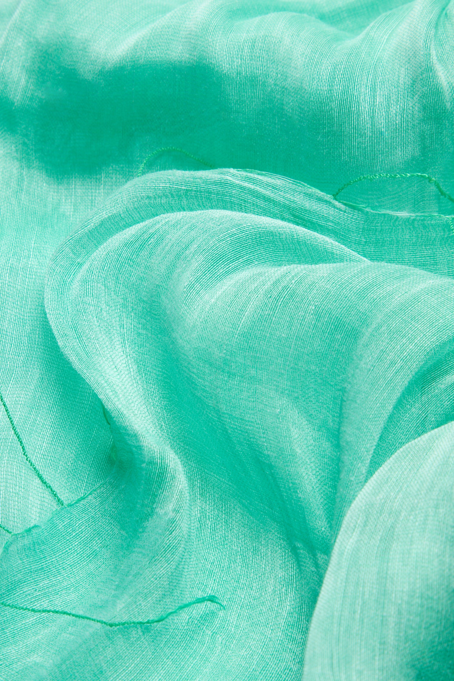 Close-up of a crumpled spearmint fabric with visible texture and light reflections, showcasing the elegance and versatility of the Spearmint Soft Linen Fringe Scarf.