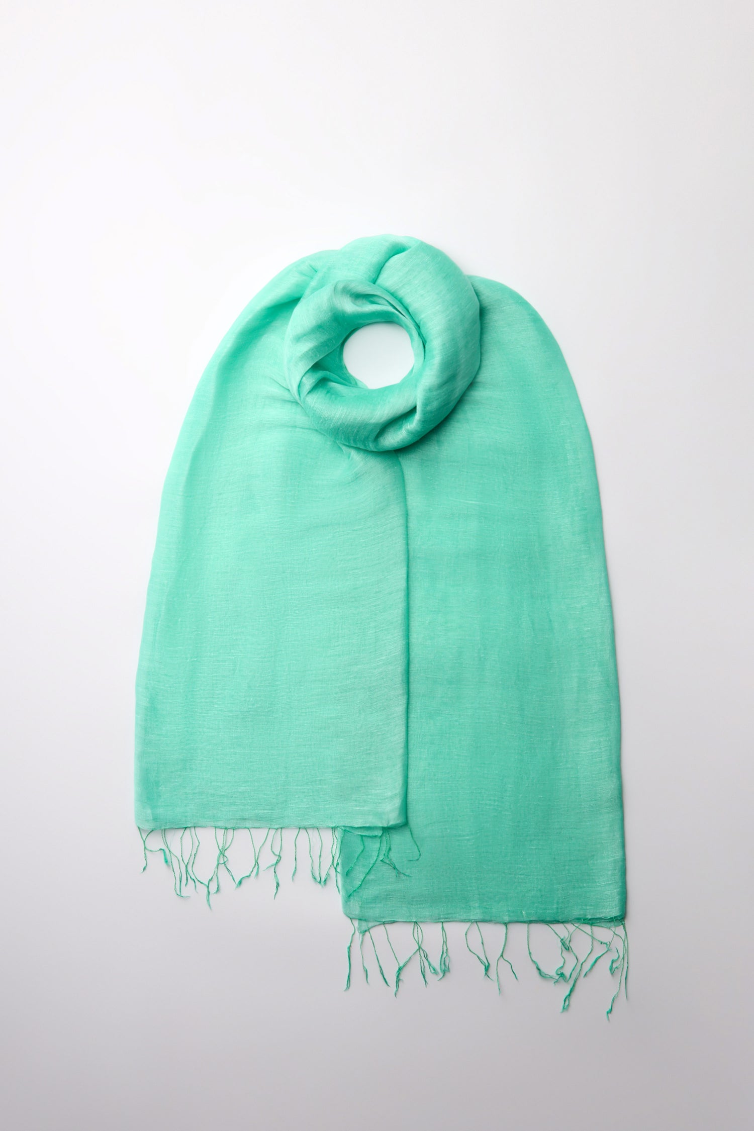 Discover the Spearmint Soft Linen Fringe Scarf in a stunning turquoise hue with delicately fringed ends. It effortlessly enhances any outfit against its crisp white backdrop.