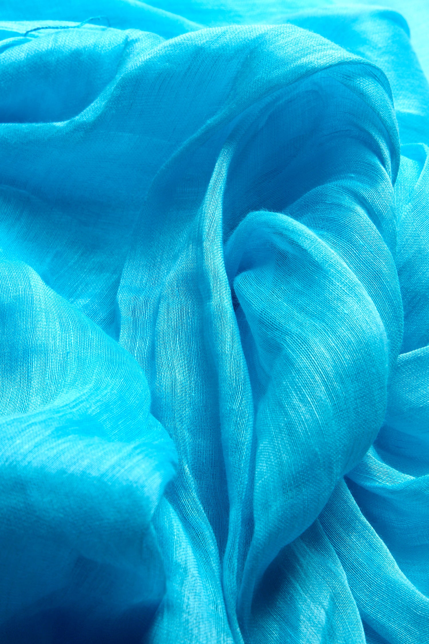 A close-up view of the Soft Linen Fringe Scarf shows its flowing blue translucent fabric, with light and shadow creating soft folds and textures reminiscent of a bohemian accessory that adds elegance to any versatile wardrobe.